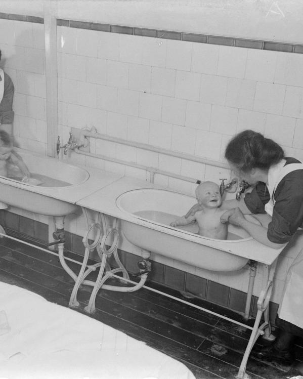 Verzorgsters van het weeshuis doen twee peuters in bad