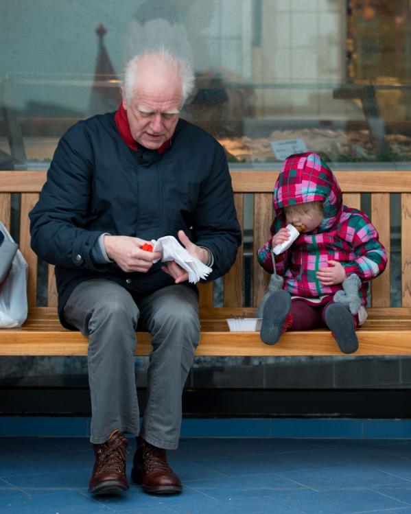 een gepensioneerde aan het eten met zijn kleindochter op een bankje