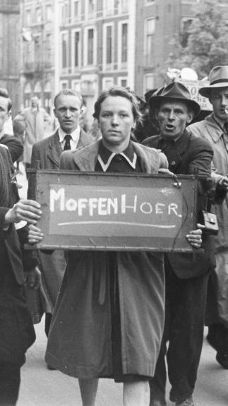 een vrouw draagt een bord met 'moffenhoer', mannen staan eromheen en wijzen ernaar