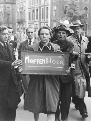 een vrouw draagt een bord met 'moffenhoer', mannen staan eromheen en wijzen ernaar