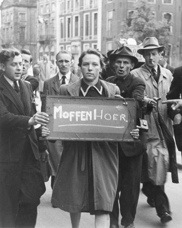 een vrouw draagt een bord met 'moffenhoer', mannen staan eromheen en wijzen ernaar