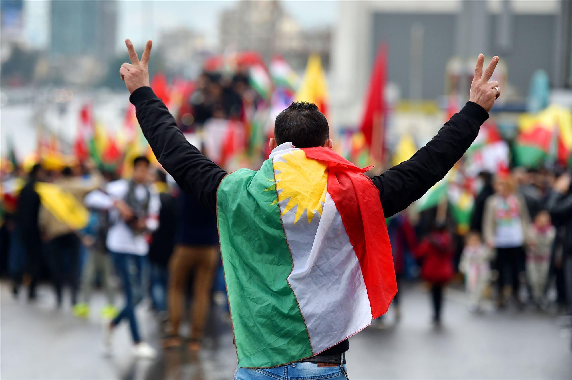 een man van de achterkant met een Koerdische vlag om zich heen en vredestekens