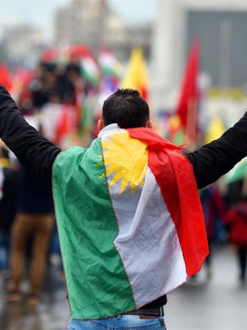 een man van de achterkant met een Koerdische vlag om zich heen en vredestekens