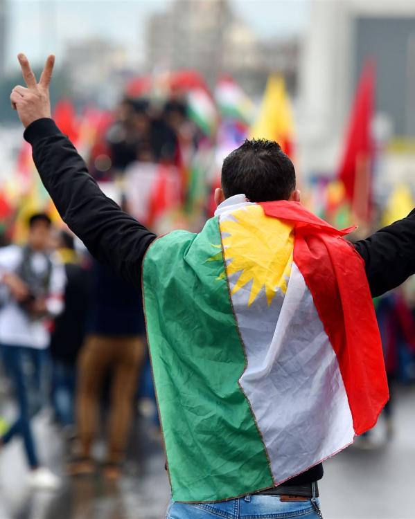 een man van de achterkant met een Koerdische vlag om zich heen en vredestekens