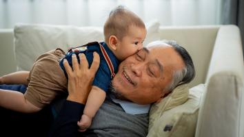 een opa ligt glimlachend op de bank met zijn kleinkind op schoot