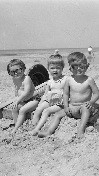 een zwart-witfoto van drie kleine jongens die samen op het strand zitten met zonnebrillen op en poseren voor de foto