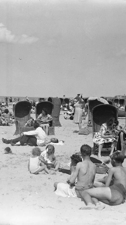 Een zwart-witfoto van mensen die op het strand zitten in de jaren 40