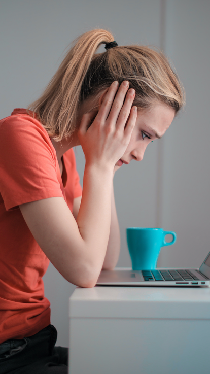 Vrouw zit met frustratie achter haar laptop.