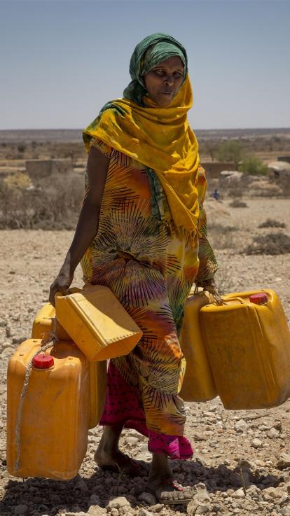 een vrouw haalt water met jerrycans vanwege de droogte in het gebied waar ze woont