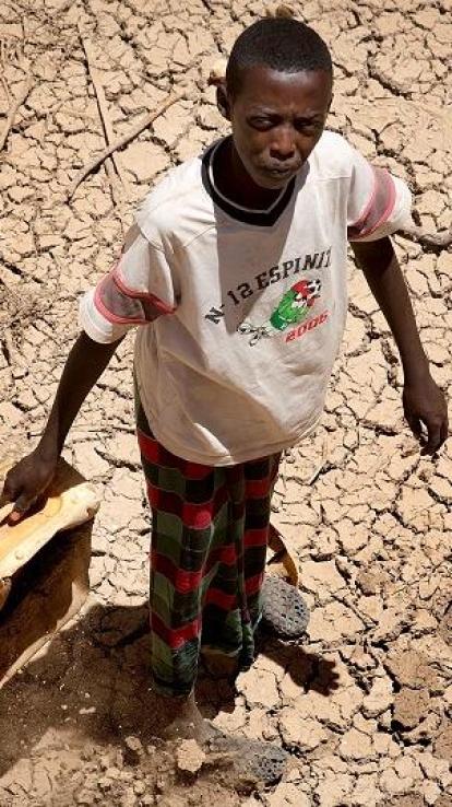 een jongen kijkt omhoog naar de fotograaf in de hitte, met op de achtergrond uitgedroogd land