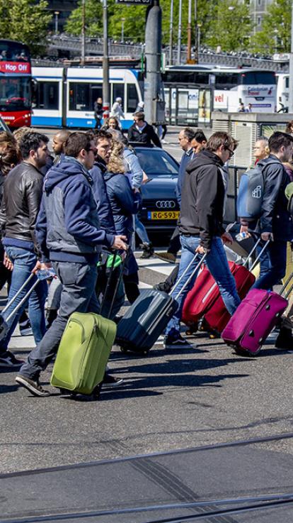 Een groep toeristen loopt met rolkoffers richting Schiphol