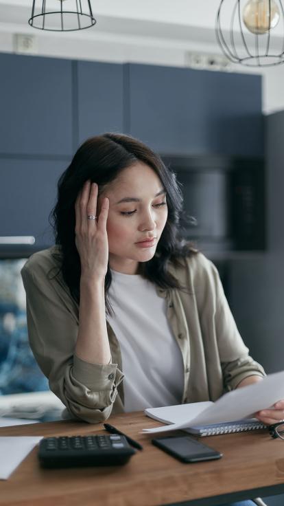 Vrouw kijkt met handen tegen haar slaap naar een rekening op tafel