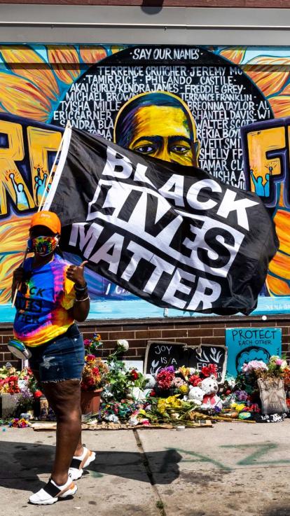 iemand poseert met een 'Black Lives Matter'-vlag voor een graffiti-kunstwerk van George Floyd en andere slachtoffers van politiegeweld in de VS
