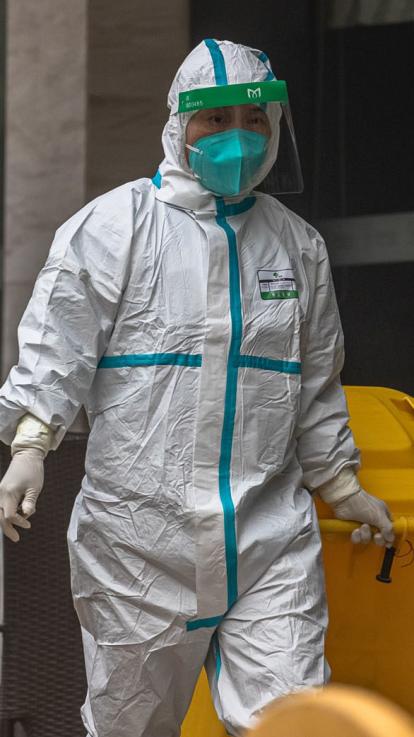 Iemand loopt in volledig afgesloten wit pak en met mondkapje voor een hotel langs met een gele container in de hand