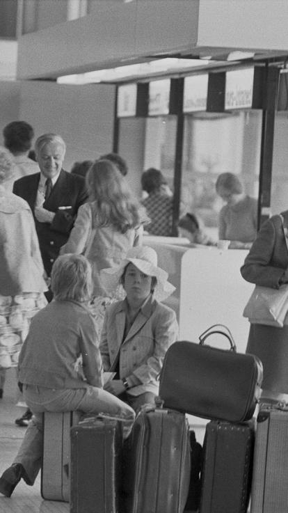 een zwart-witfoto van wachtende mensen in de vertrekhal van Schiphol in de jaren 70