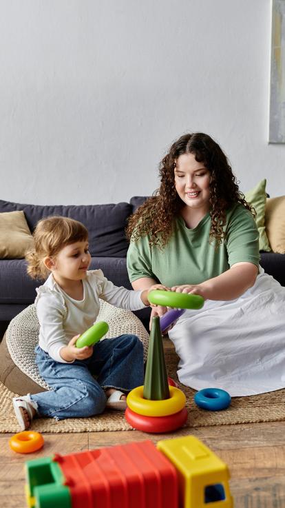 Een moeder speelt met haar kind voor de bank met een kleurrijk torentje met ringen