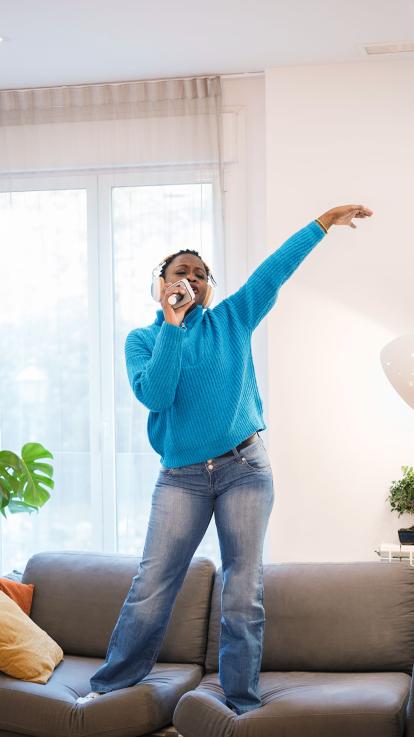 Een vrouw staat met koptelefoon en microfoon te zingen op de bank