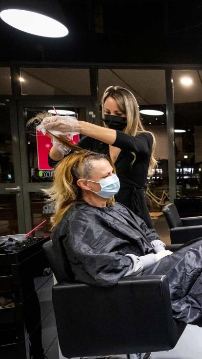 een kapper in coronatijd aan het werk met een mondkapje op, net als de klant