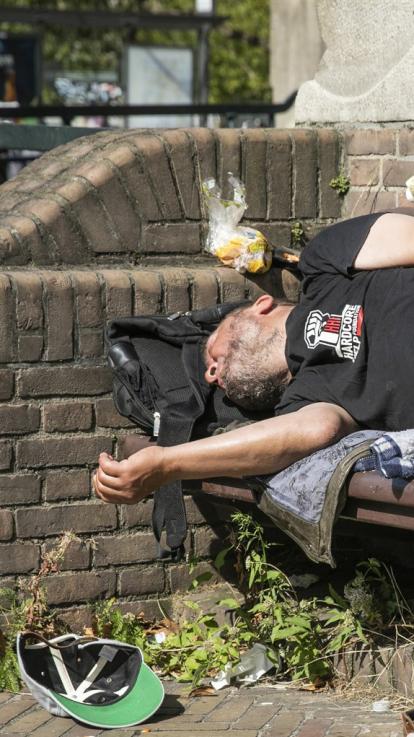 een dakloze man ligt op een bankje te slapen