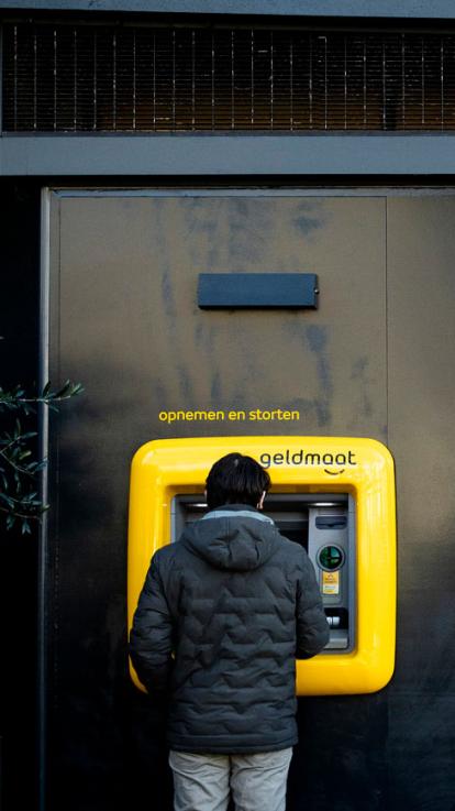 Iemand staat bij een geldautomaat voor het opnemen en storten van geld