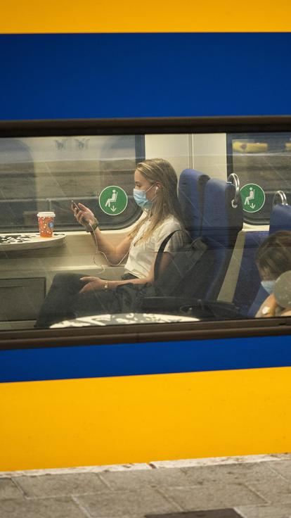 Foto door treinraam naar binnen waar vrouwen met mondkapje op in zitten. 