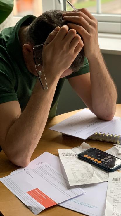 een man met zijn handen in zijn haren en allemaal documenten, bonnetjes en een rekenmachine voor hem op tafel