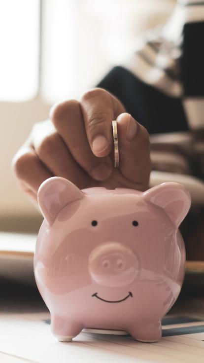een hand stopt een muntje in een varkens-spaarpotje