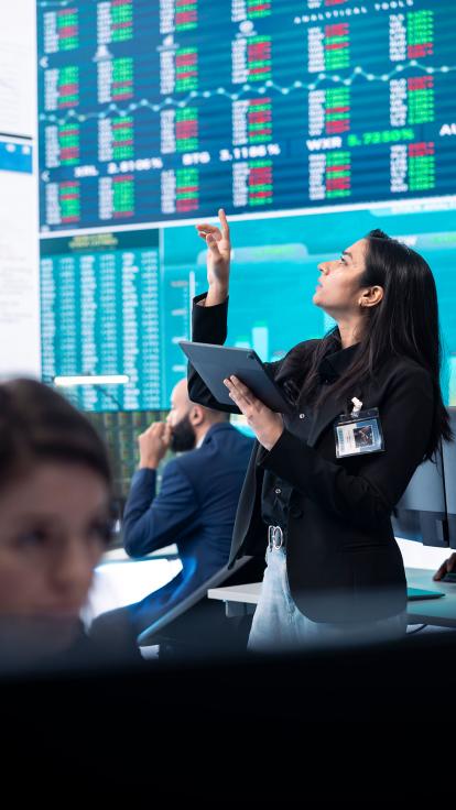 Een leidinggevende wijst naar digitale borden met informatie over aandelen op een beurs