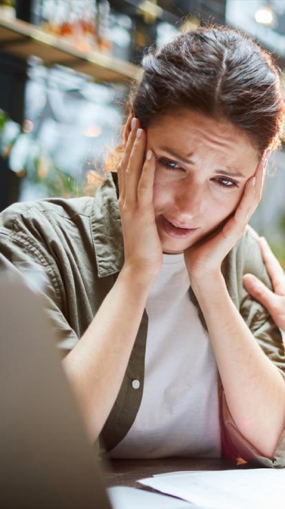Een vrouw kijkt verschrikt naar haar laptop met haar handen aan de zijkanten van haar gezicht