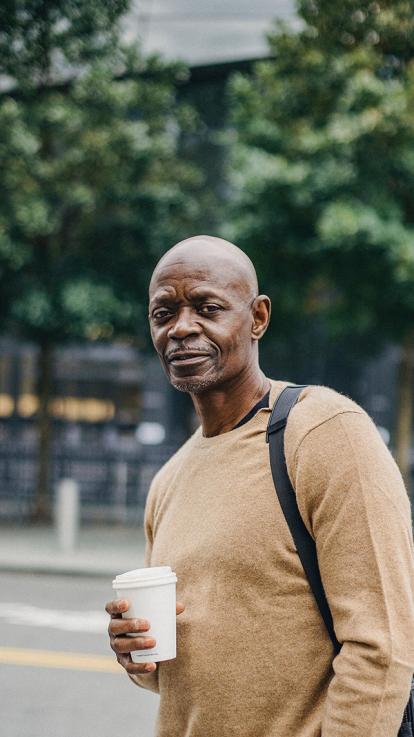Kale man buiten met koffie in zijn hand kijkt de camera in 
