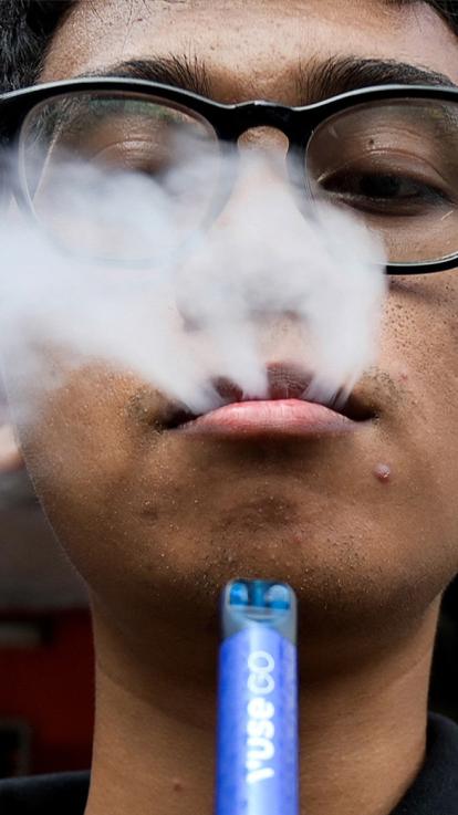 Minderjarige jongen blaast rook van een blauwe vape uit