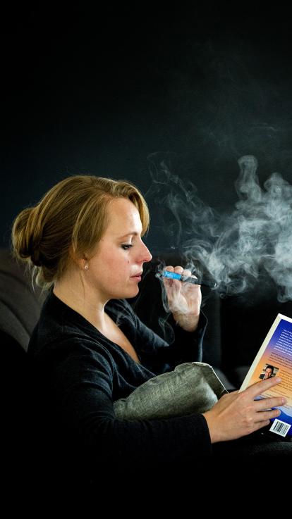 vrouw rookt een e-sigaret terwijl ze een boek leest