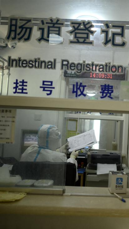 een laboratoriummedewerker loopt met beschermende kleding, bril en mondkapje door het lab