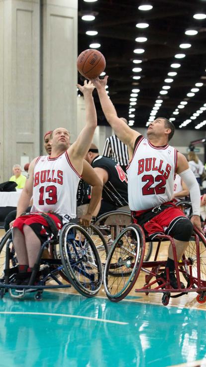 Twee mannen in rolstoel strijden om de bal in de lucht.