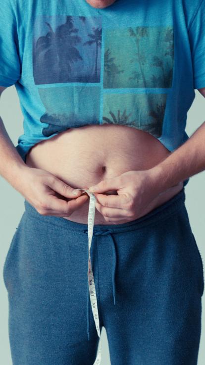 man meet met meetlint de omtrek van zijn buik en kijkt of hij is afgevallen