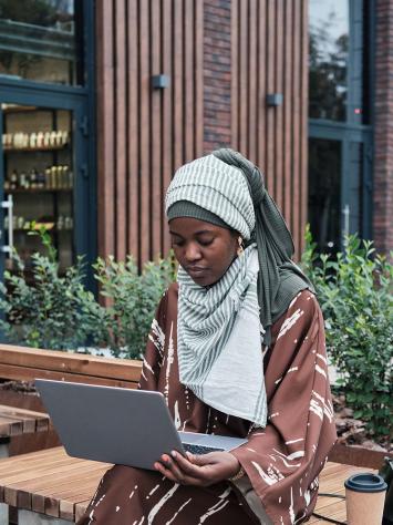 Een vrouw aan het werk op haar laptop op een bankje buiten