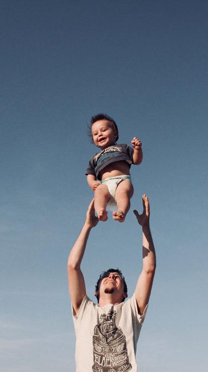 Man tilt klein jongetje op in de lucht, ze kijken gelukkig en blij