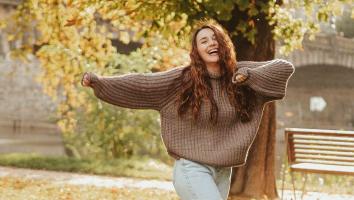 Vrouw maakt dansbeweging voor boom met herfstbladeren