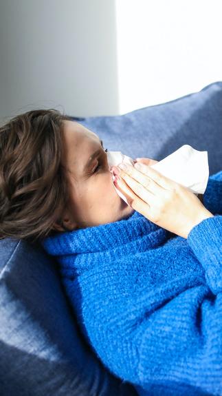 een vrouw met dikke trui niest in een zakdoekje