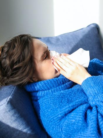 een vrouw met dikke trui niest in een zakdoekje