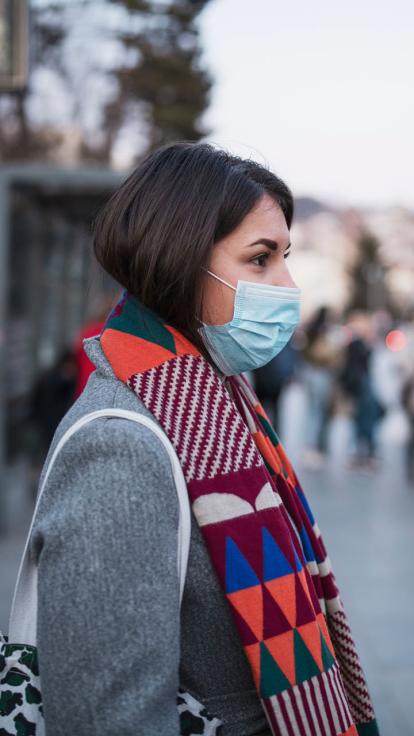 Vrouw staat met mondkapje op de trein te wachten.