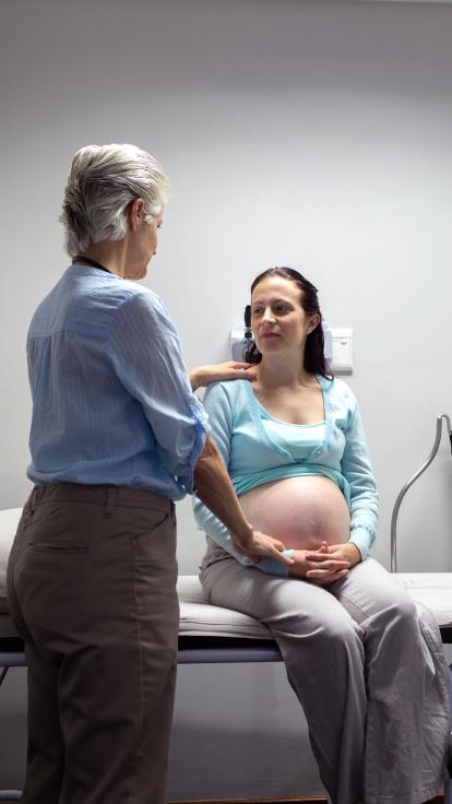 Een zwangere vrouw zit op een onderzoekstafel terwijl een arts haar onderzoekt