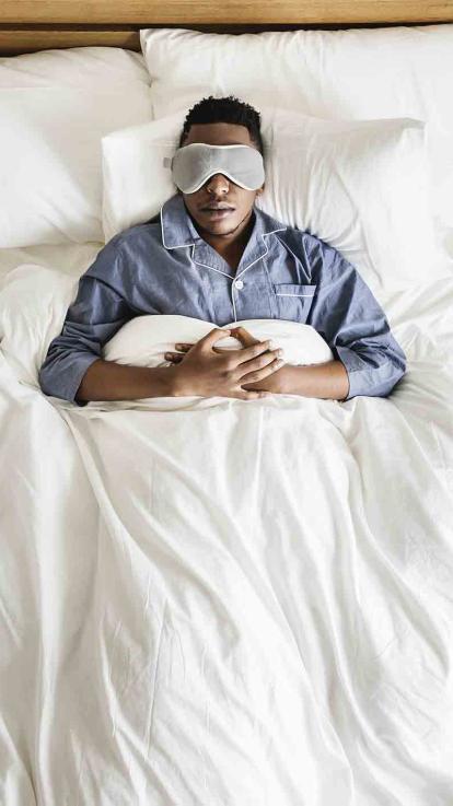 Man ligt met slaapmasker op in bed