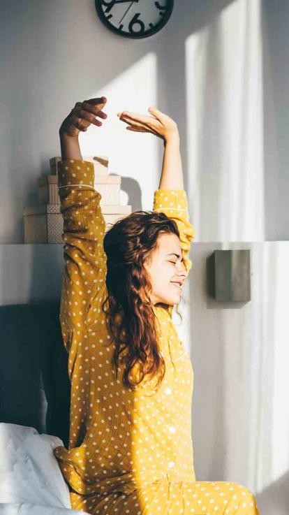 Vrouw wordt wakker, strekt haar armen en kijkt in het zonlicht
