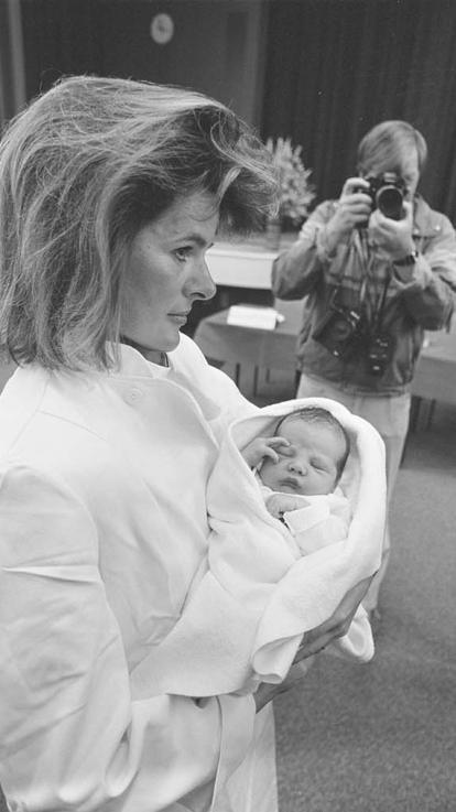 Een zwart-witfoto van een moeder die haar baby vasthoudt met fotografen op de achtergrond