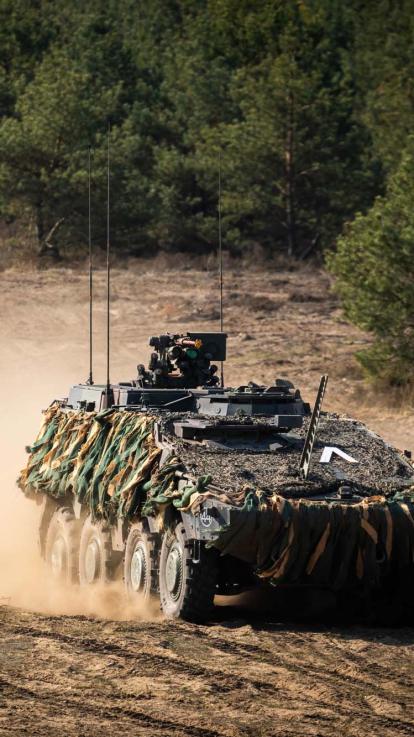 Een tank van de landmacht bij een militaire oefening, met veel stuivend zand erachter