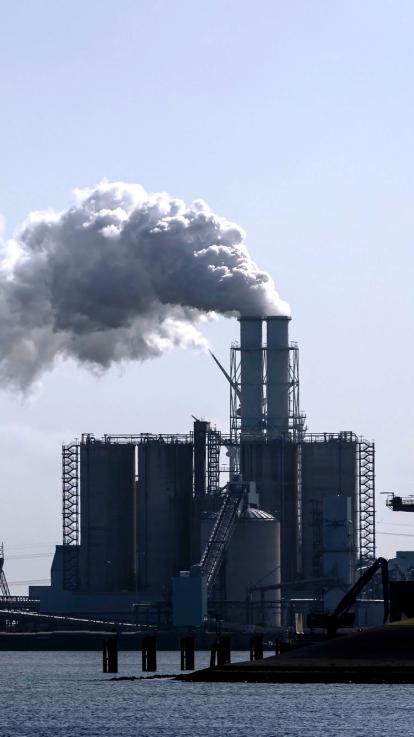 Een elektriciteitscentrale met water ervoor en met dikke rookpluimen erbovenuit 