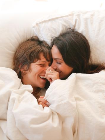 Twee vrouwen knuffelend en lachend in bed 