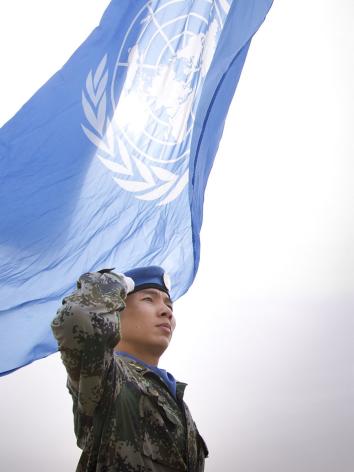 een blauwhelm bij de vlag van de verenigde naties