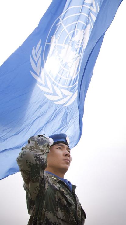 een blauwhelm bij de vlag van de verenigde naties
